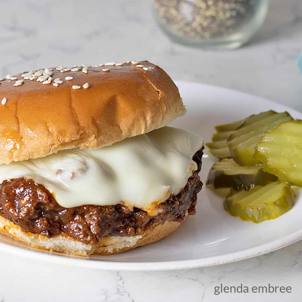 Best Sloppy Joes Recipe - sloppy joe sitting on a white plate with dill pickle chips - easy recipes - family recipes