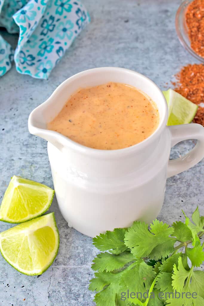 Southwest Dressing in White Pitcher on concrete counter with limes, cilantro, spices and blue print fabric