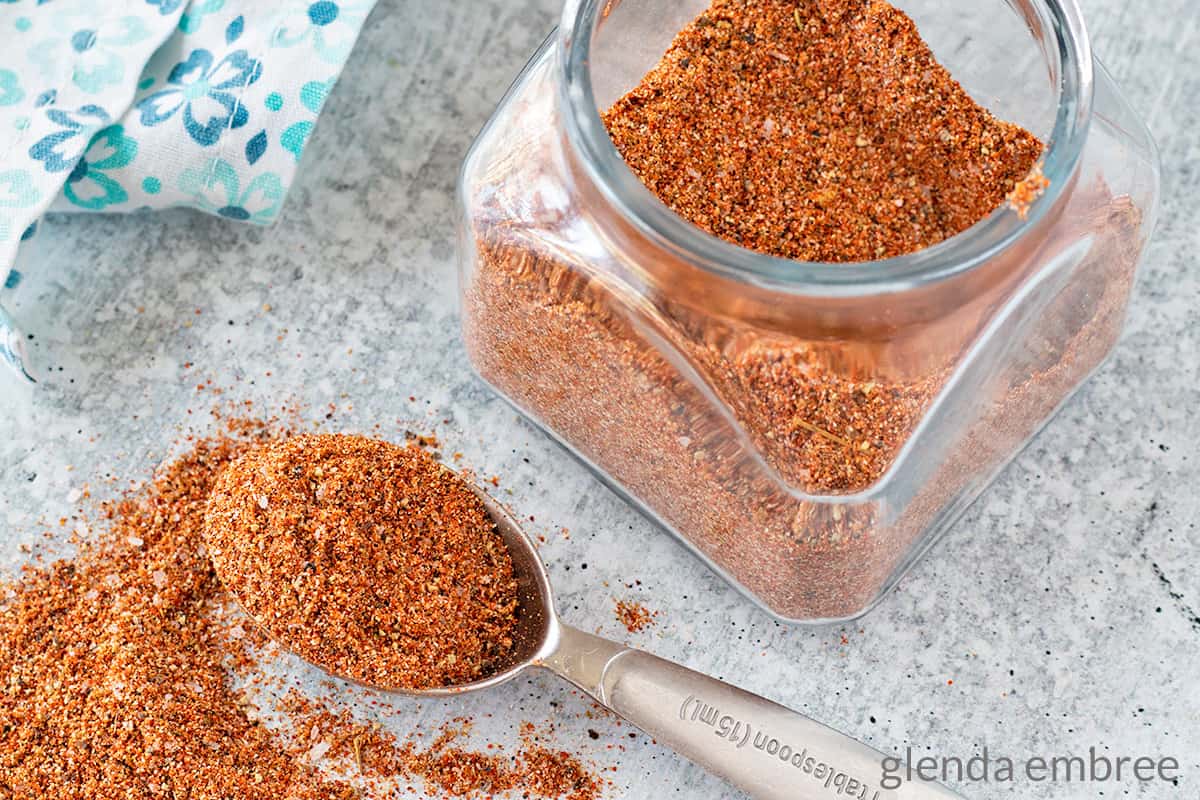 Southwest Seasoning Blend in a jar and spilling out of a measuring spoon on a concrete counter top