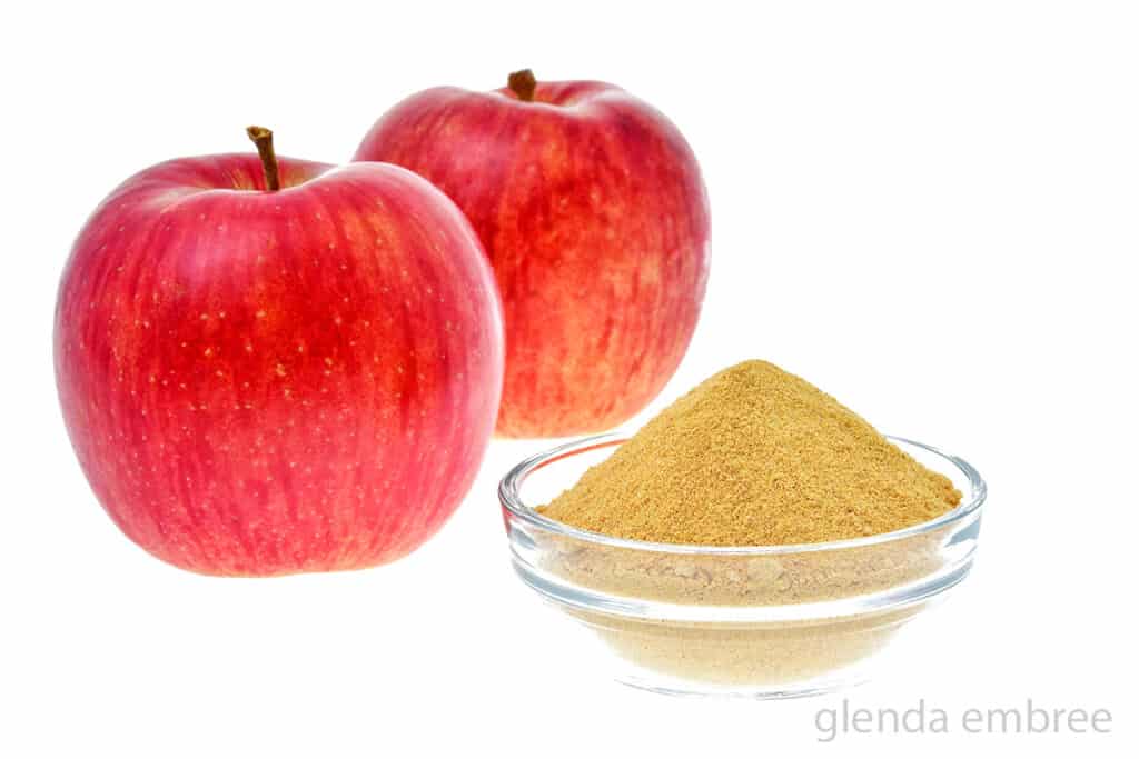 two red apples next to a bowl of powdered pectin