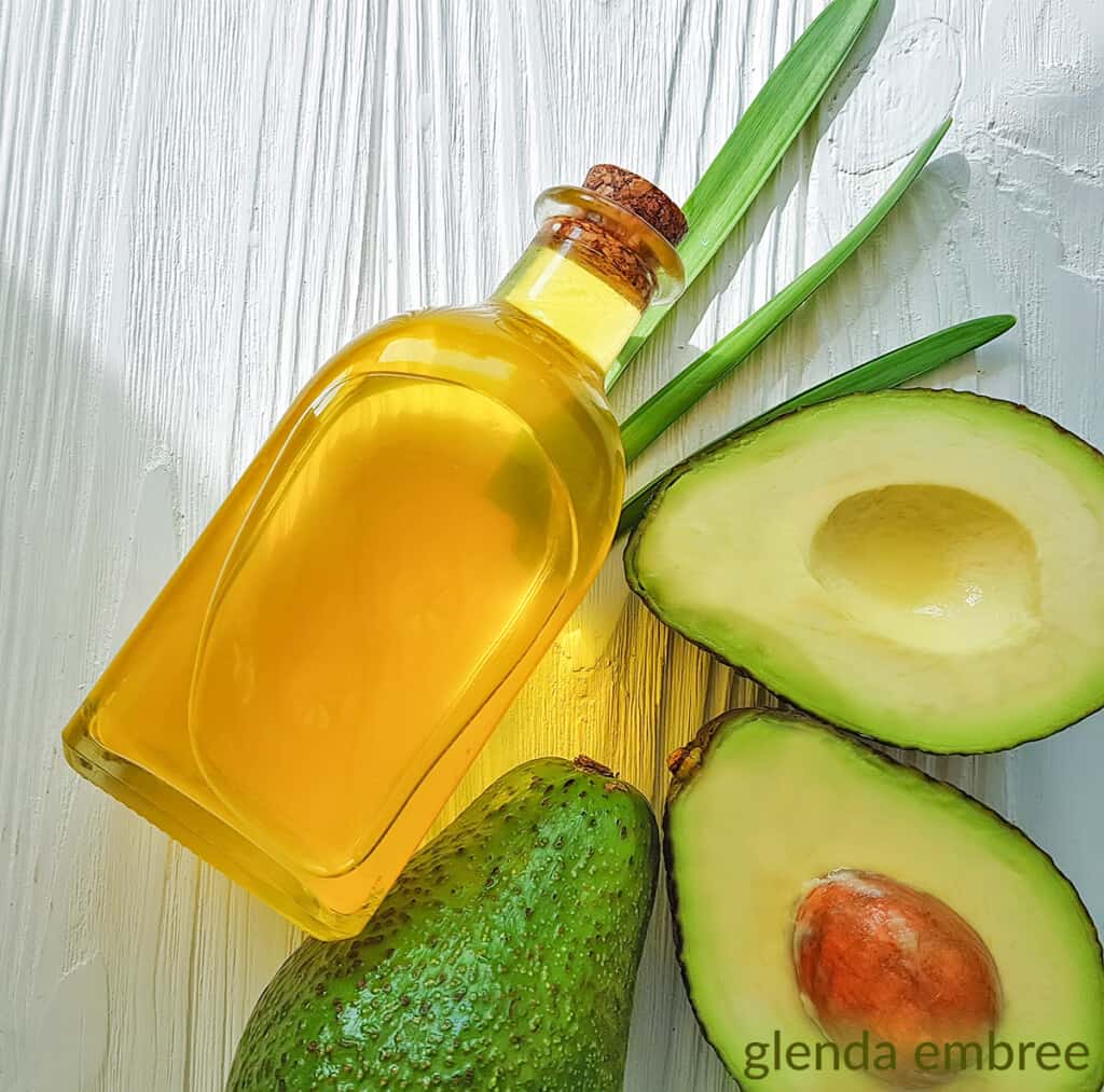 avocado cut in half laying on a table next to a whole avocado and bottle of avocado oil