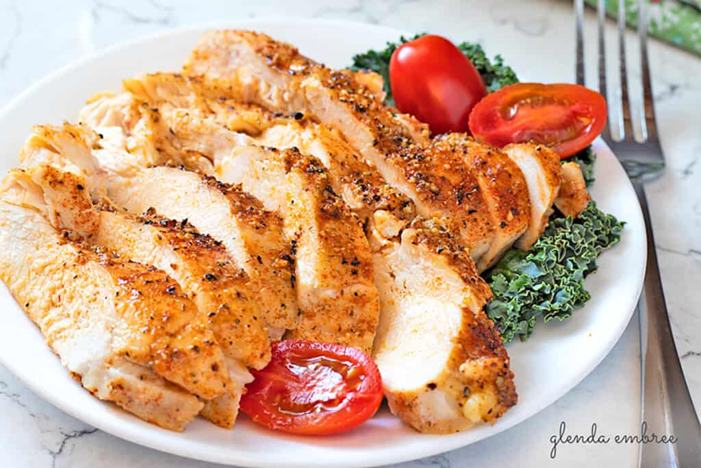Perfect Baked Chicken Breasts on a white plate with kale and tomatoes