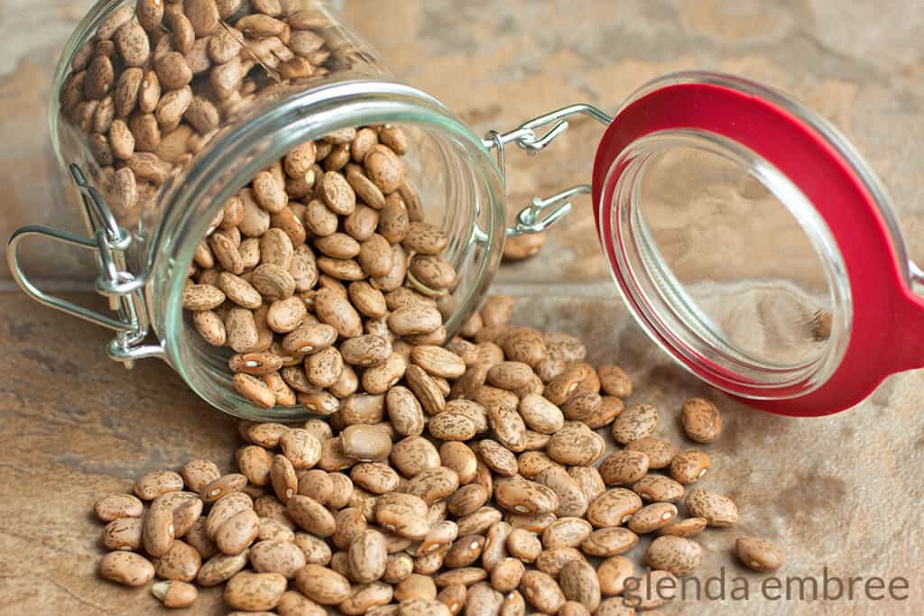 dry pinto beans spilling out of a mason jar onto a wooden counter