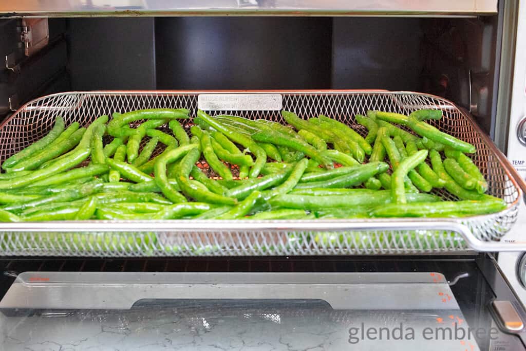 fresh green beans tossed in oil and salt, arranged in a single layer in air fryer basket
