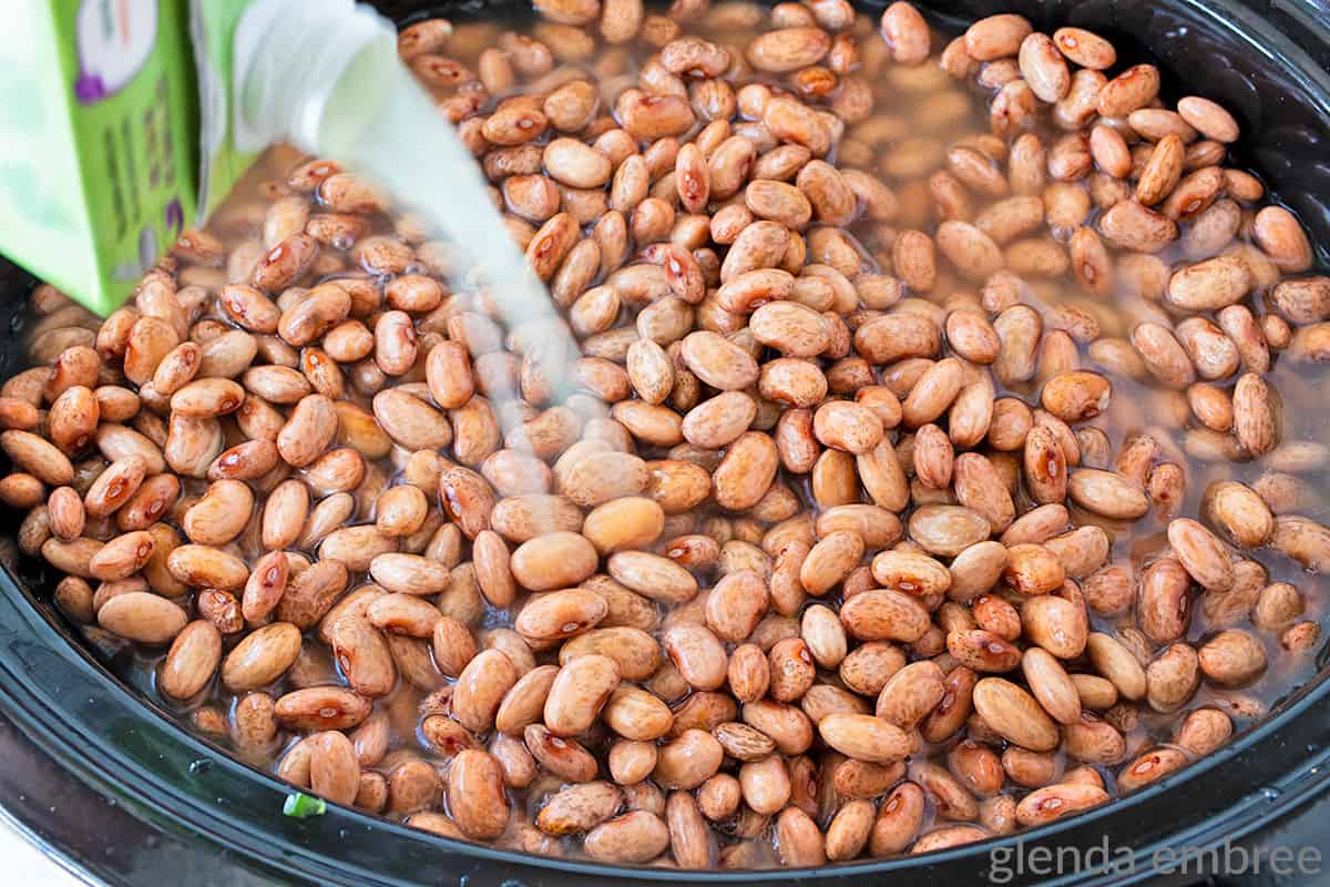 pouring broth over pinto beans in a slow cooker for charro beans recipe