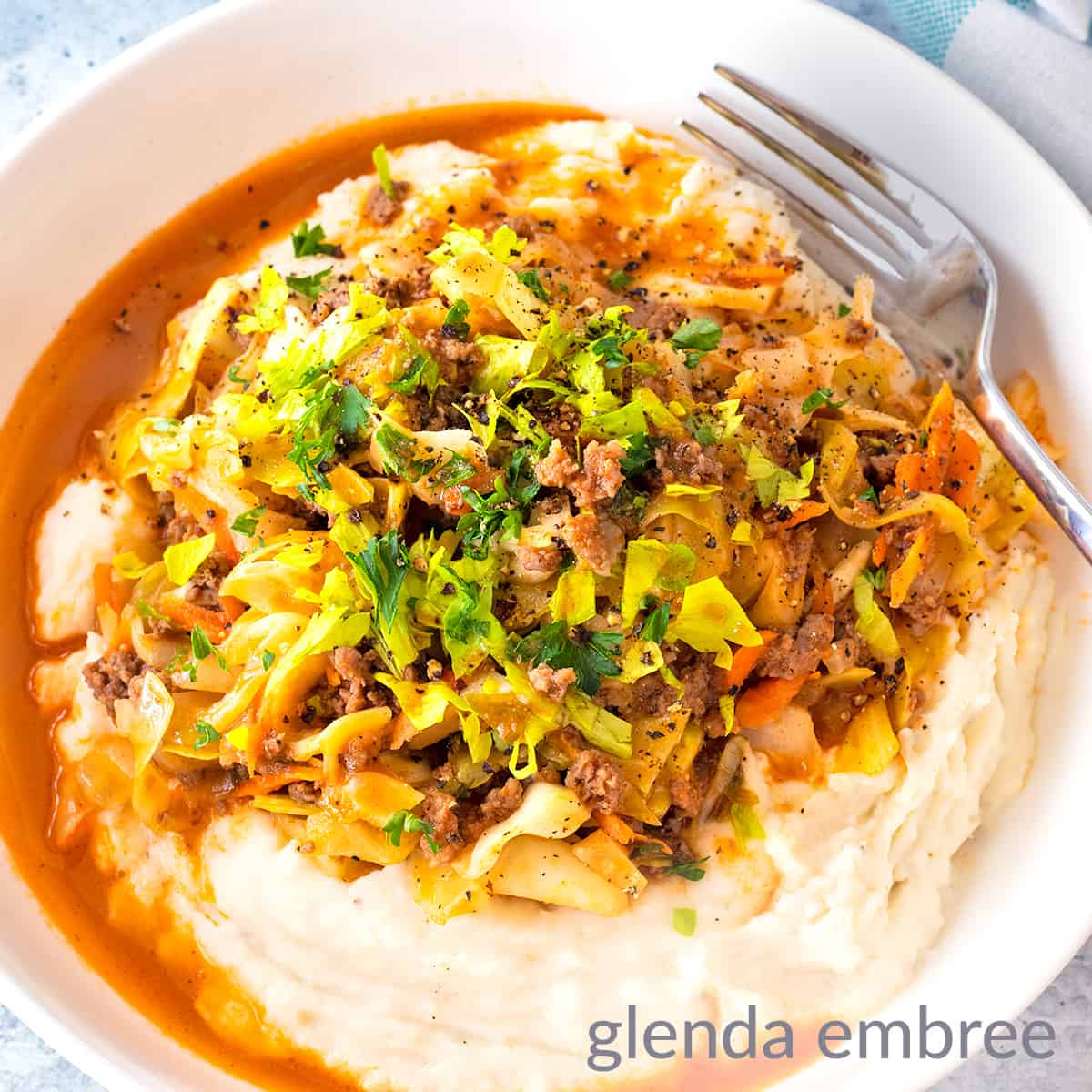 Ground Beef and Cabbage over Mashed Potatoes in a white stoneware bowl sitting on a concrete counter