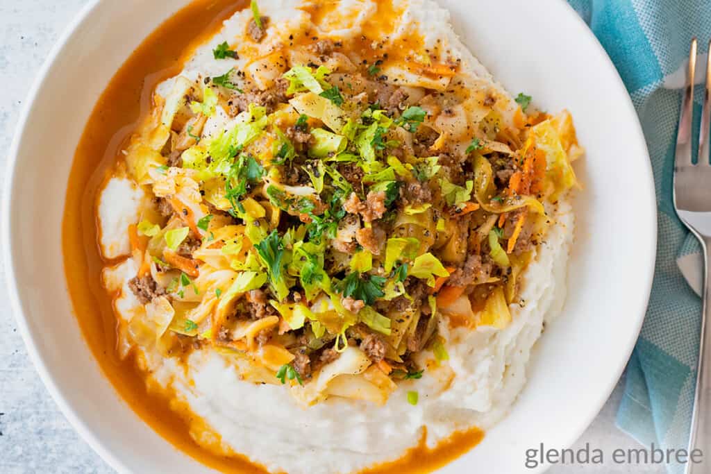 Ground Beef and Cabbage over Mashed Potatoes in a white stoneware bowl sitting on a concrete counter
