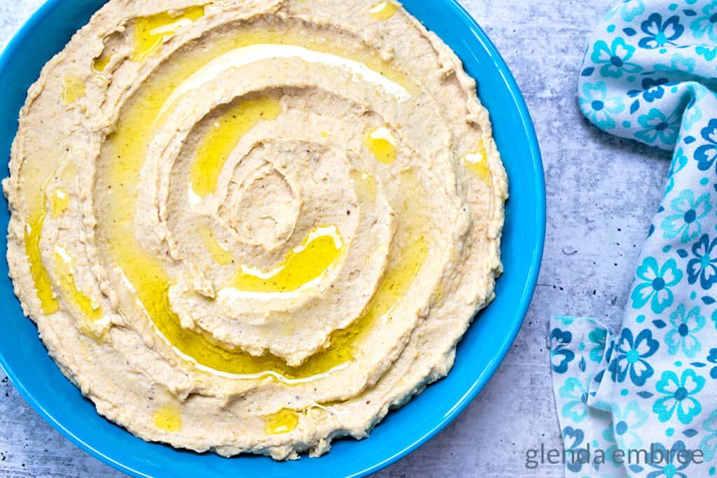 Creamy Hummus Recipe served plain in a blue stoneware bowl with a drizzle of olive oil