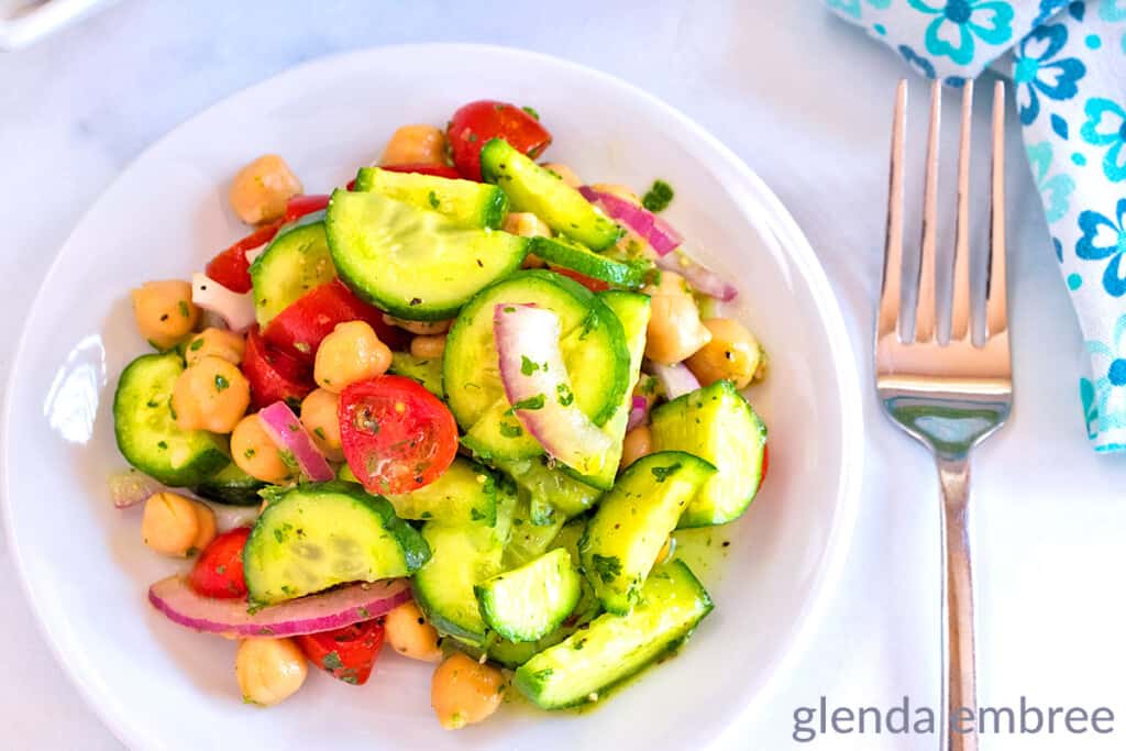 Mediterranean Cucumber Tomato Salad on a white plate next to a fork and blue and white print napkin