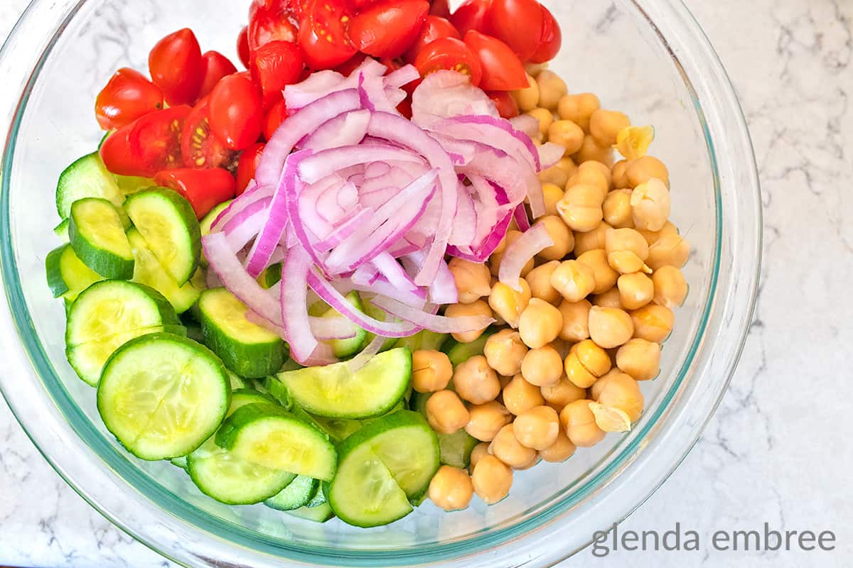 chopped tomatoes, red onion slivers, chickpeas, sliced cucumber in a clear glass mixing bowl