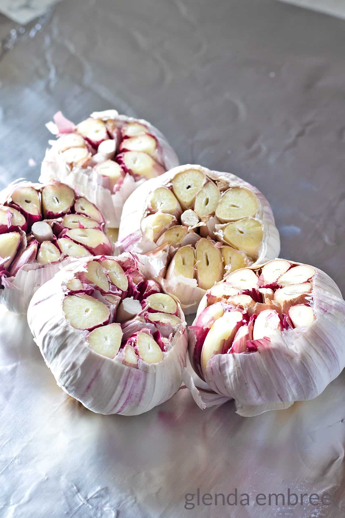5 heads raw garlic with tops removed sitting on a sheet of foil
