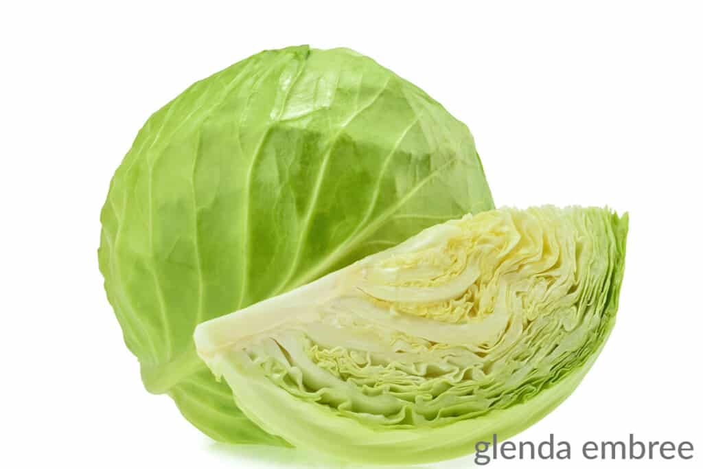 head of cabbage with a cut wedge of cabbage sitting in front of it