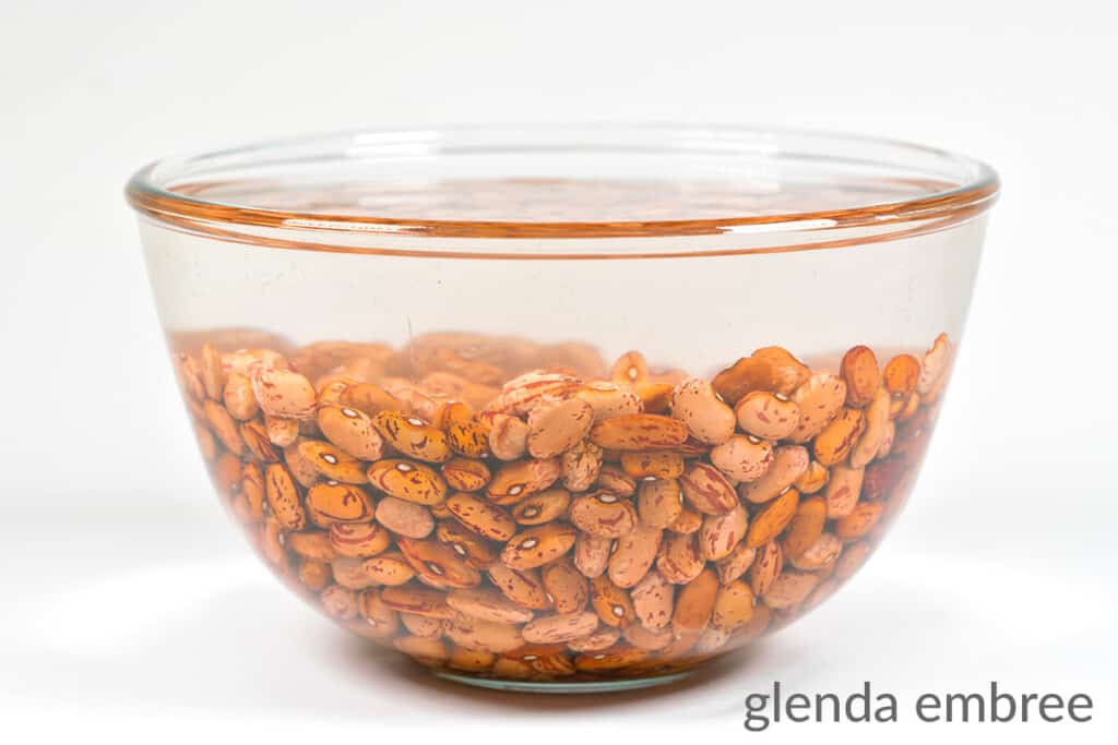 soaking dry pinto beans in a clear glass mixing bowl