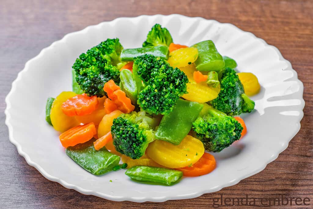 steamed vegetables on a white plate - broccoli, snap peas, carrots and squash