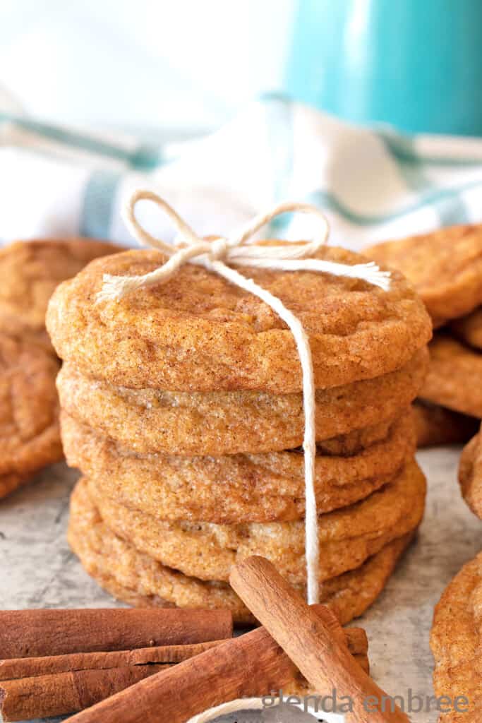 chai spiced pumpkin snickerdoodles on a concrete counter with cinnamon sticks and one stack of cookies tied with a piece of white twine