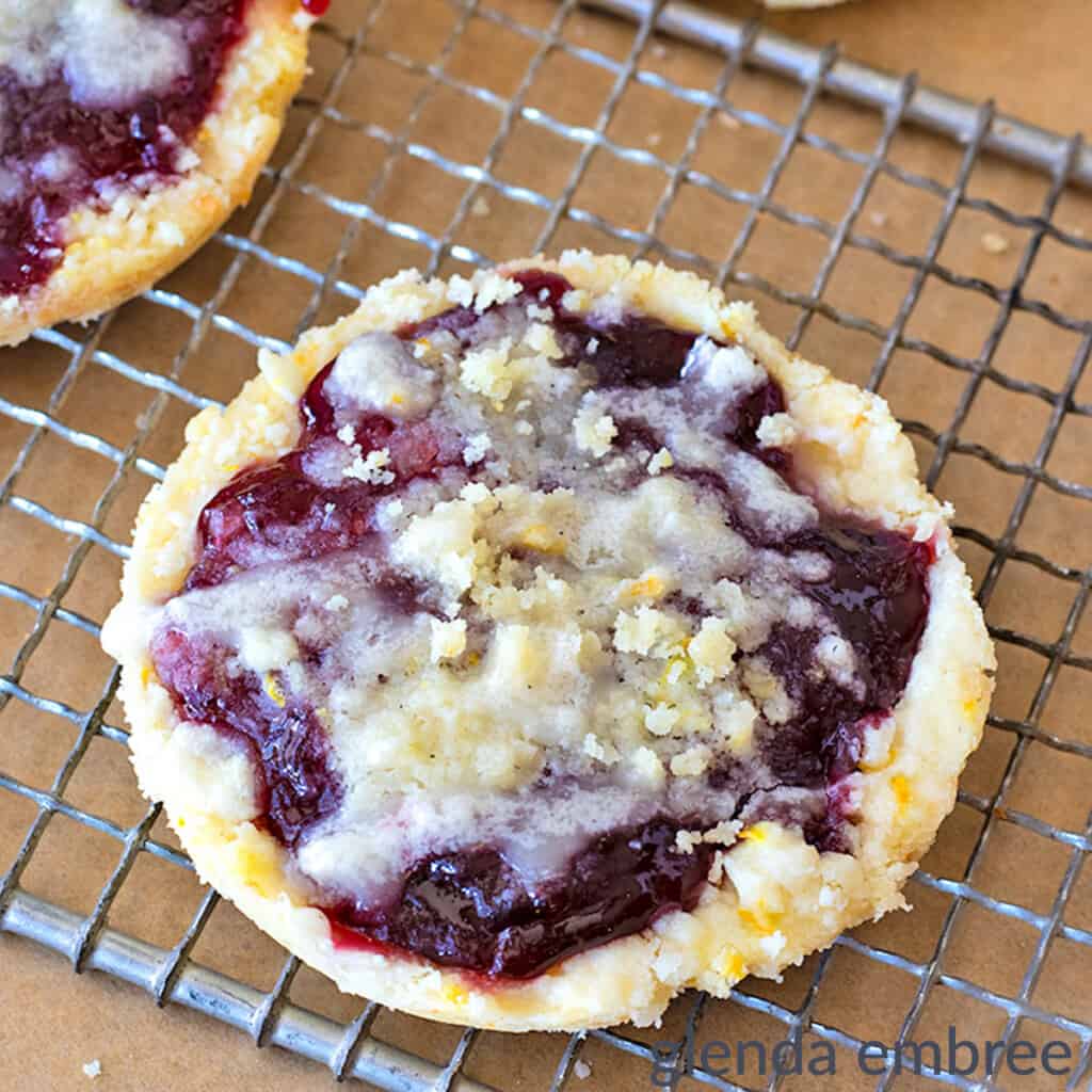 copycat Costco raspberry crumble cookies on a wire rack with more cookies on brown paper and on a wooden cutting board in the background