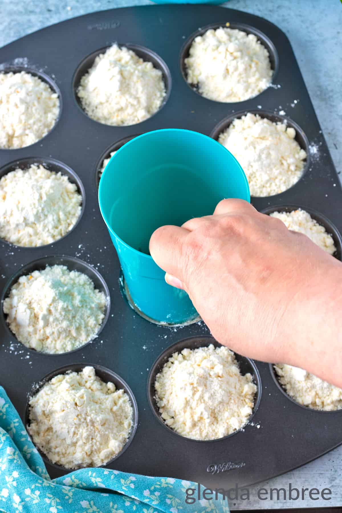 Using the bottom of a cup to press the shortbread cookie dough crumbles into a solid disk.