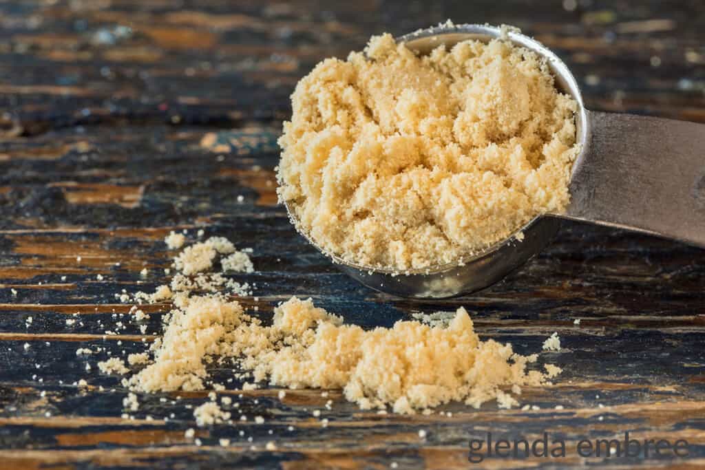 Malted Milk Powder spilling out of a teaspoon onto a wooden table