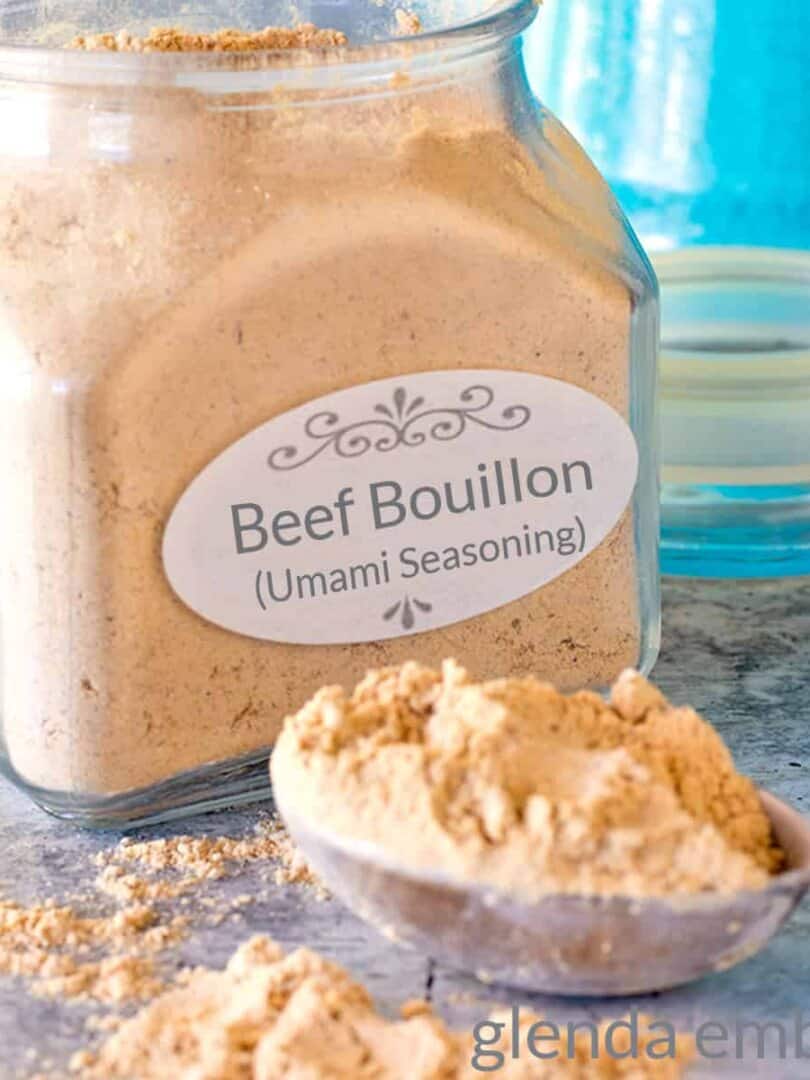 Homemade beef bouillon in an apothecary jar on a concrete counter. A heaping Tablespoon of bouillon sits on the counter in front of the jar.