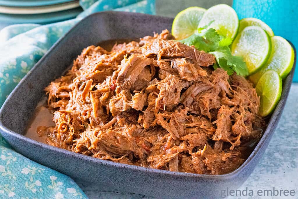 Mexican Shredded beef in a with lime slices and cilantroin a square, gray stoneware bowl