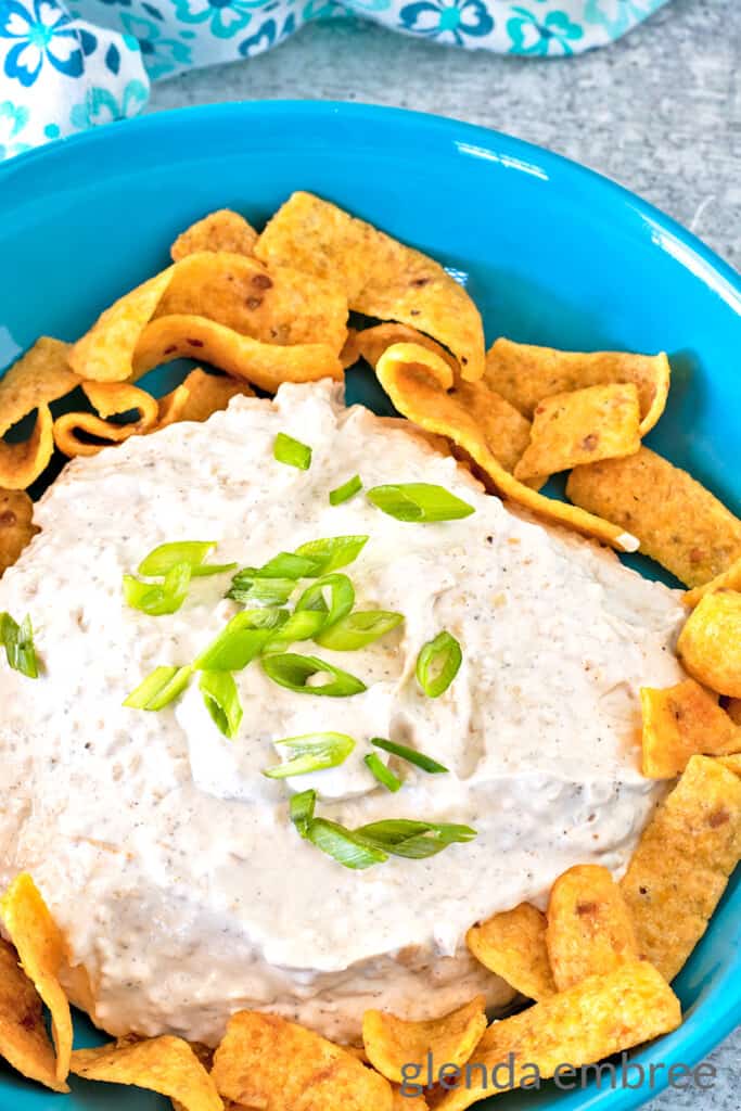 homemade onion dip in a blue ceramic bowl, surrounded by corn chips