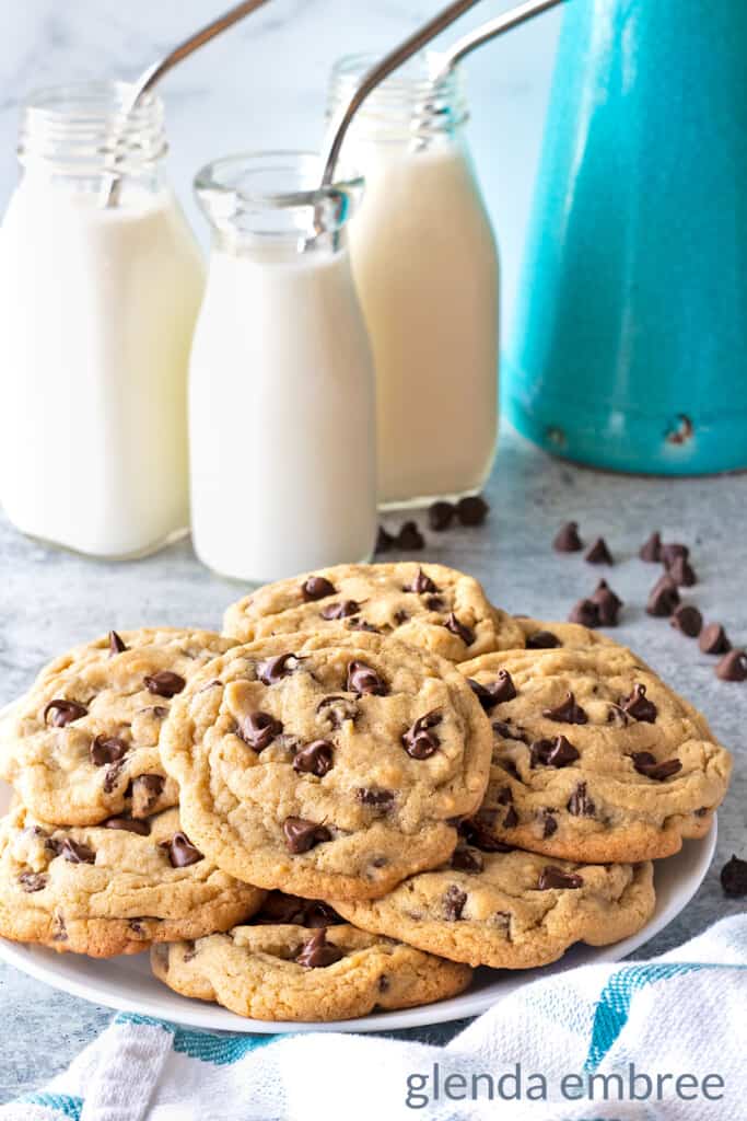 Small Batch Chocolate Chip Cookies on a white plate sitting on a concrete countertop with 3 milk bottles that have steel straws
