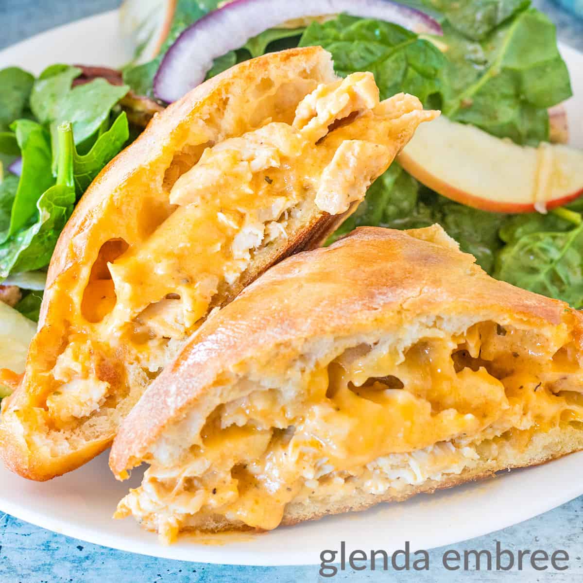 Buffalo Ranch Chicken Melts on a white plate with spinach salad. Plate is on a concrete countertop.