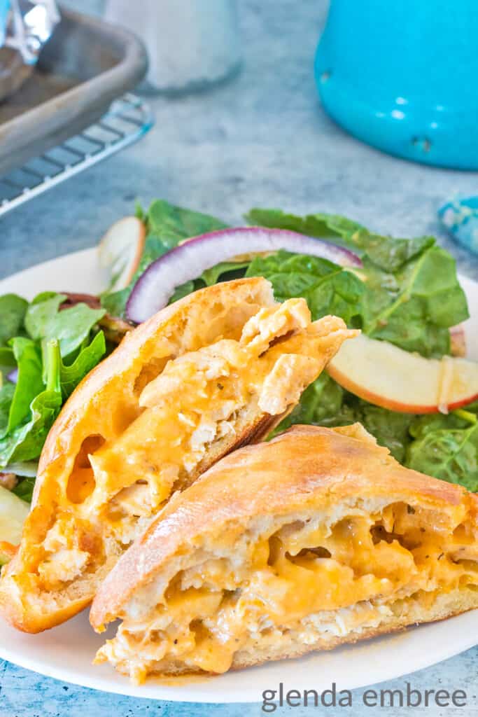 Buffalo Ranch Chicken Melts on a white plate sitting on a concrete countertop.  Sandwiches are served with spinach and apple salad.