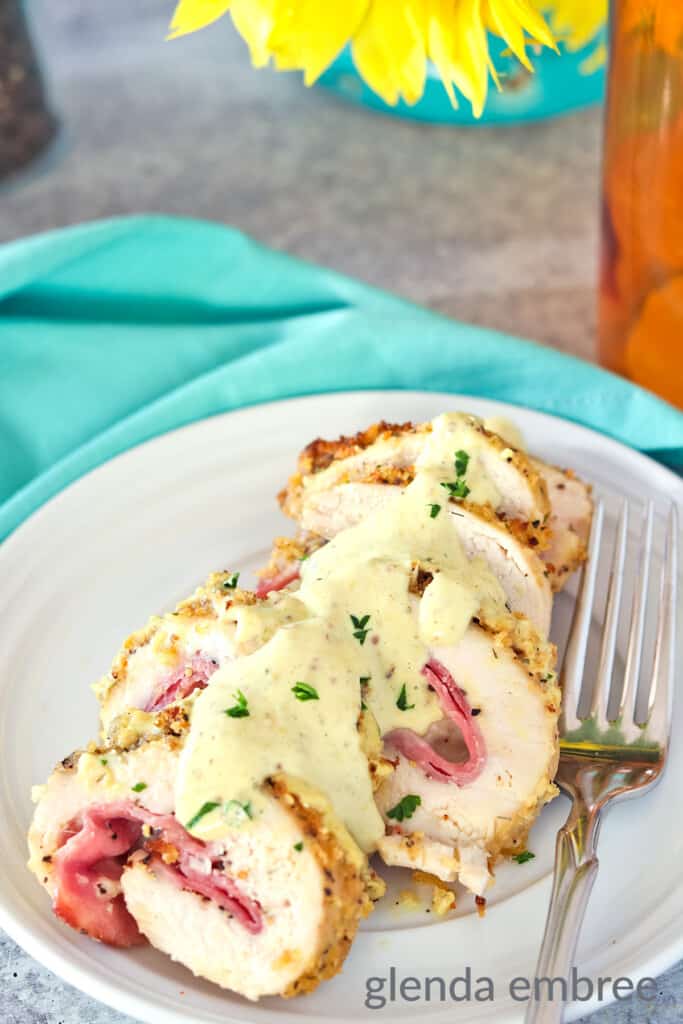 Chicken Cordon Bleu sliced on a white plate with creamy stone ground mustard sauce drizzled over the slices