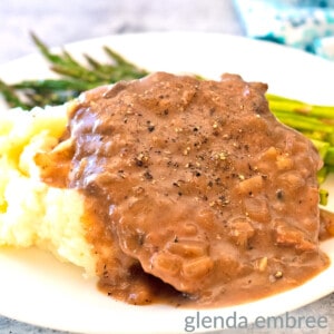 crock pot cube steak on a white plate with mashed potatoes and asparagus