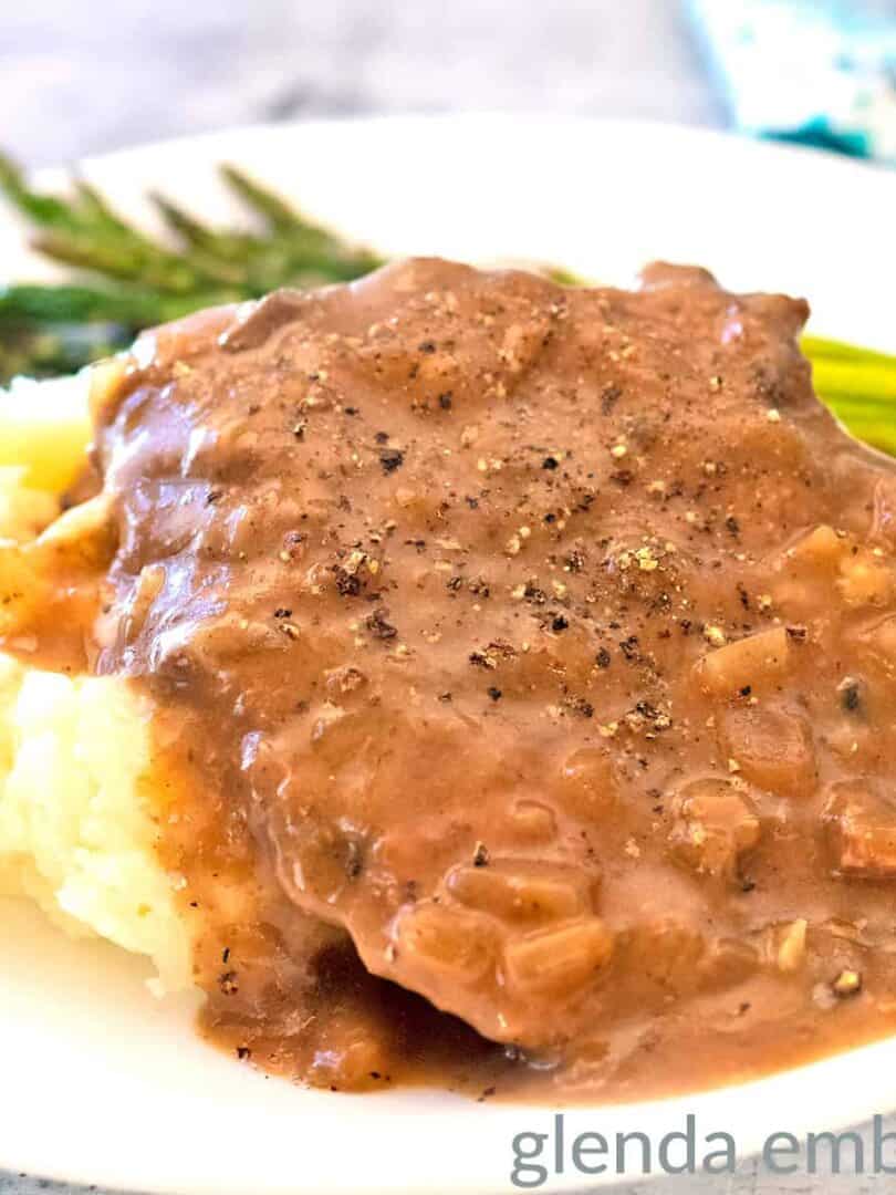 Crock pot cube steak on a white plate with mashed potatoes and asparagus.