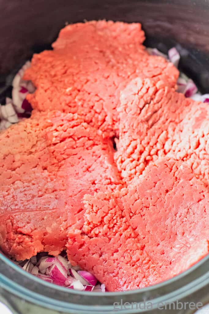 Raw cubed steak layered over a bed of minced red onion in a slow cooker