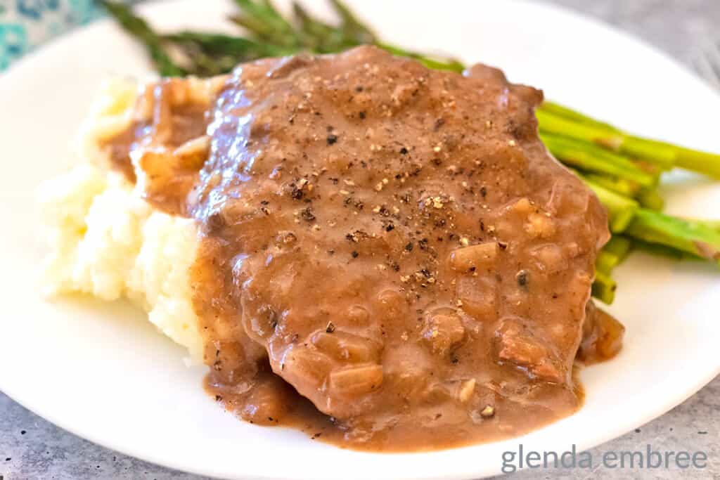 crock pot cube steak on a white plate with mashed potatoes and asparagus