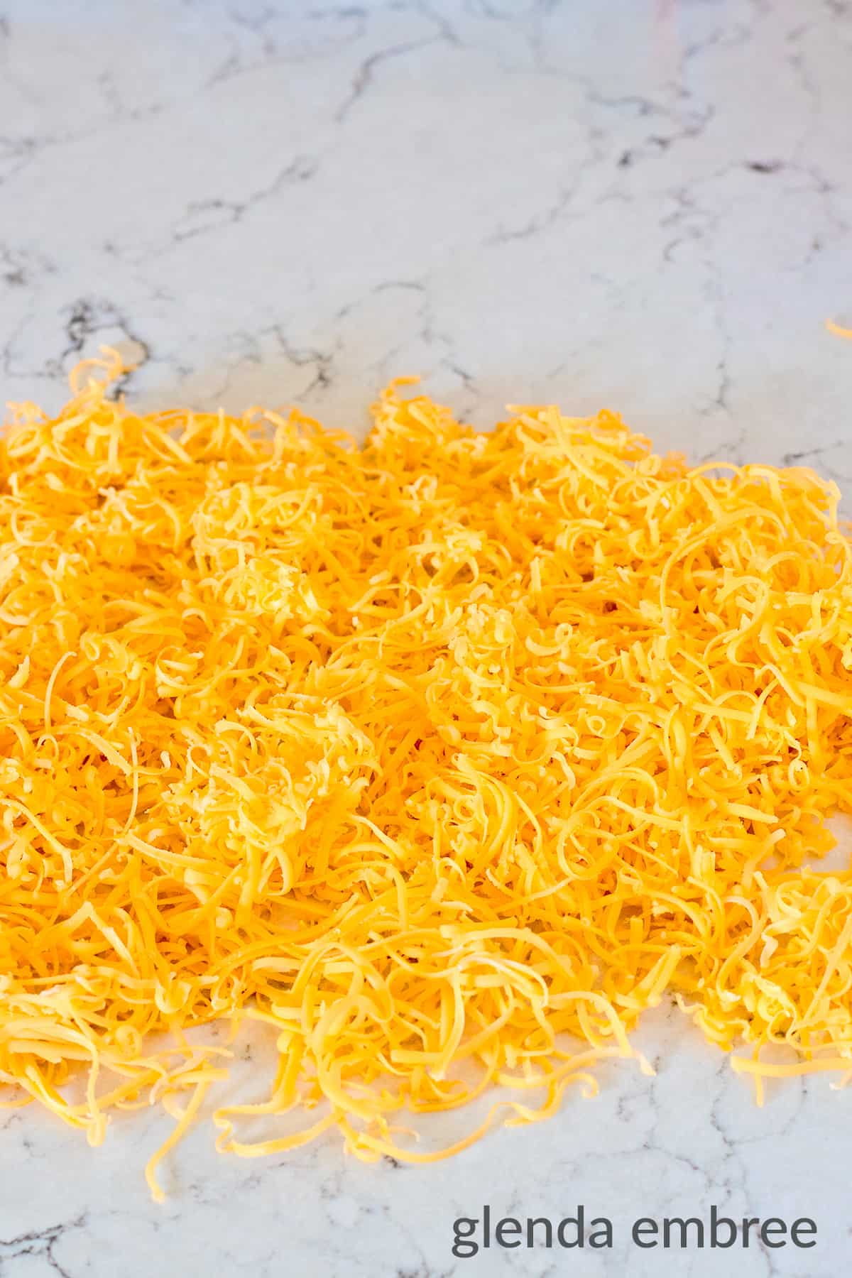 a pile of grated Cheddar cheese on a marble counter