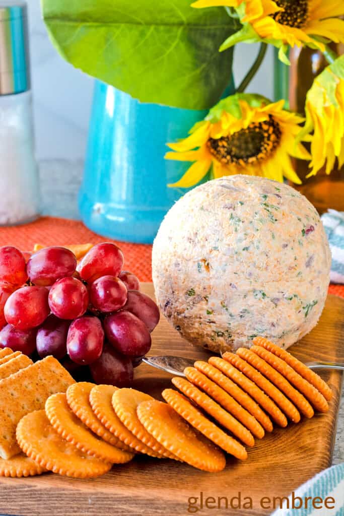Bacon and Pineapple Cheese Ball on a Wooden Cutting Board with an assortment of crackers and red grapes