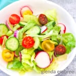 House Salad in a white ceramic bowl on a concrete countertop. There is a fork lying next to the bowl witha turquoise fabric napkin.