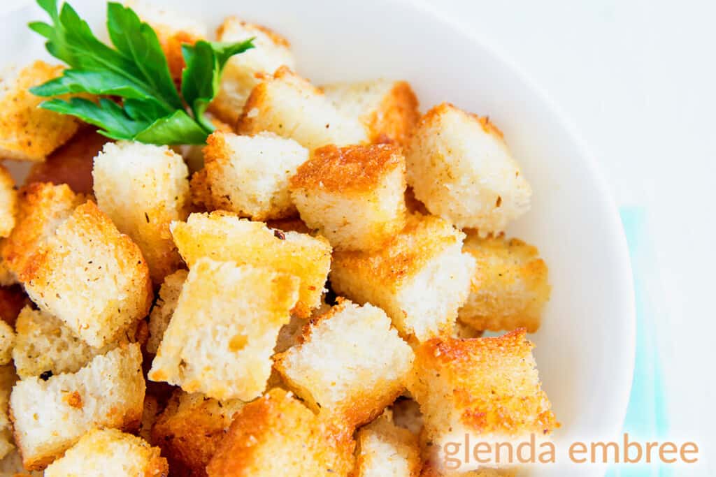 croutons in a white bowl with a sprig of flat leaf parsley