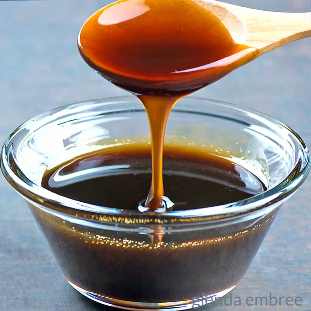 Molasses dripping off a wooden spoon into a clear glass bowl of molasses