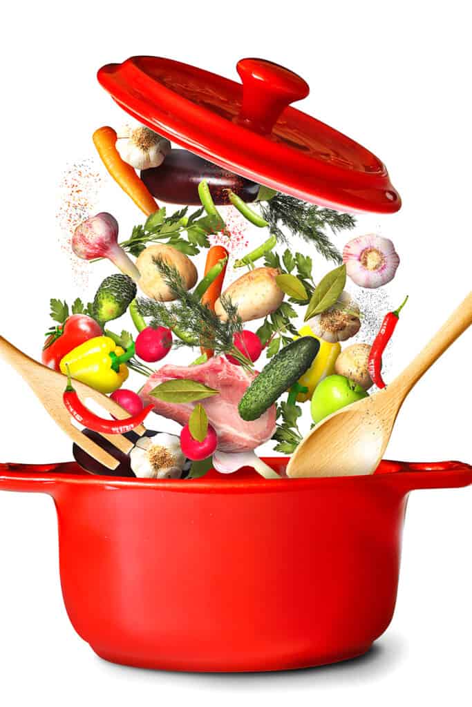 a red pot with falling vegetables, herebs and seasonings hovering above the pot and the pot lid above the vegetables