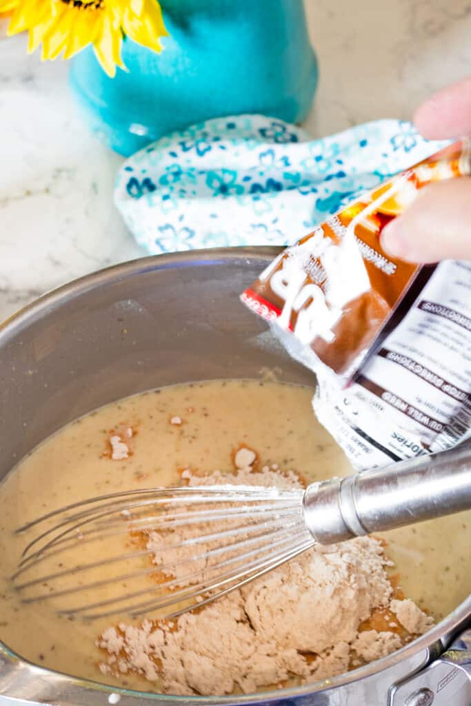 adding turkey gravy mix packet to cooking pot with gravy and a wire whisk in it