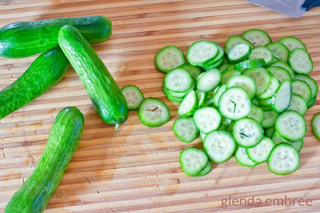 Mini cucumbers, aka Persian cucumbers, on a wooden cutting board with alongside cucumber slices.