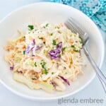 Best Easy Coleslaw Recipe served in a white bowl on a marble countertop. A blue and white print fabric napkin is in the background.