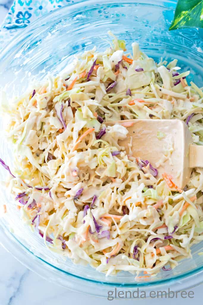 Cabbage slaw mixed with coleslaw dressing in a clear white bowl on a marble countertop