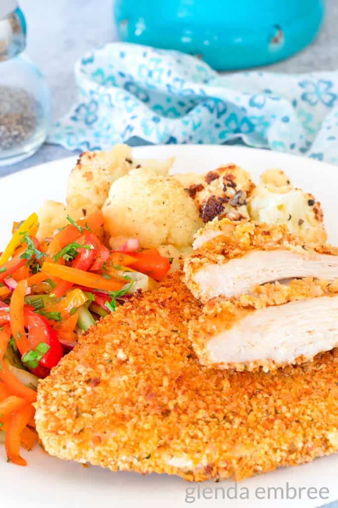 Air Fryer Chicken Cutlets on a white plate with roasted cauliflower and bell pepper salad