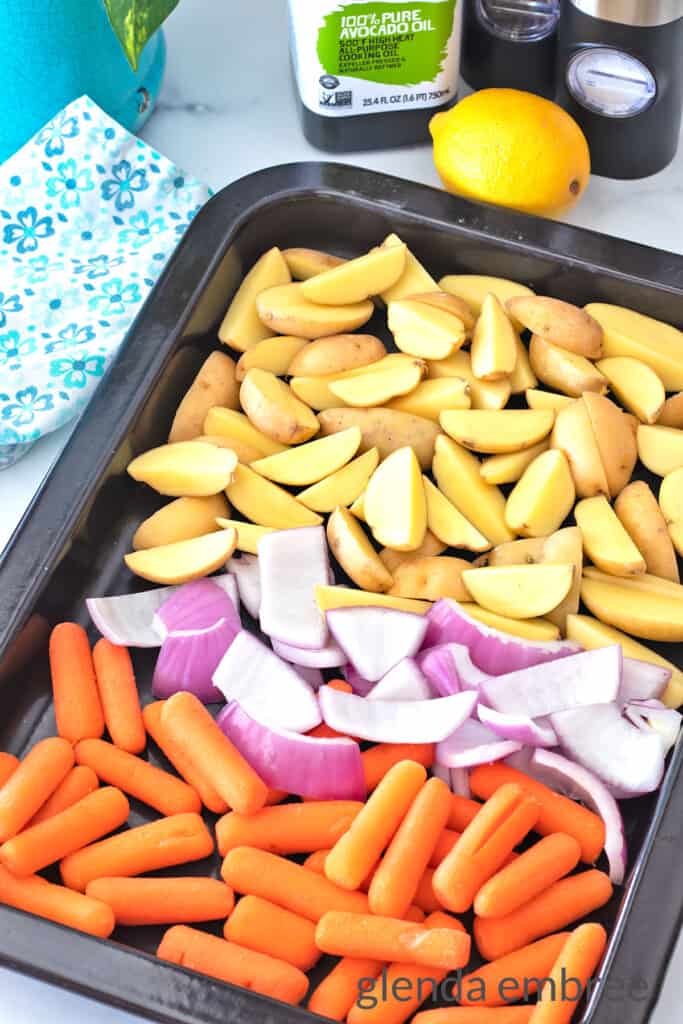 Raw baby potatoes, baby carrots and onion chunks in a black roasting pan.