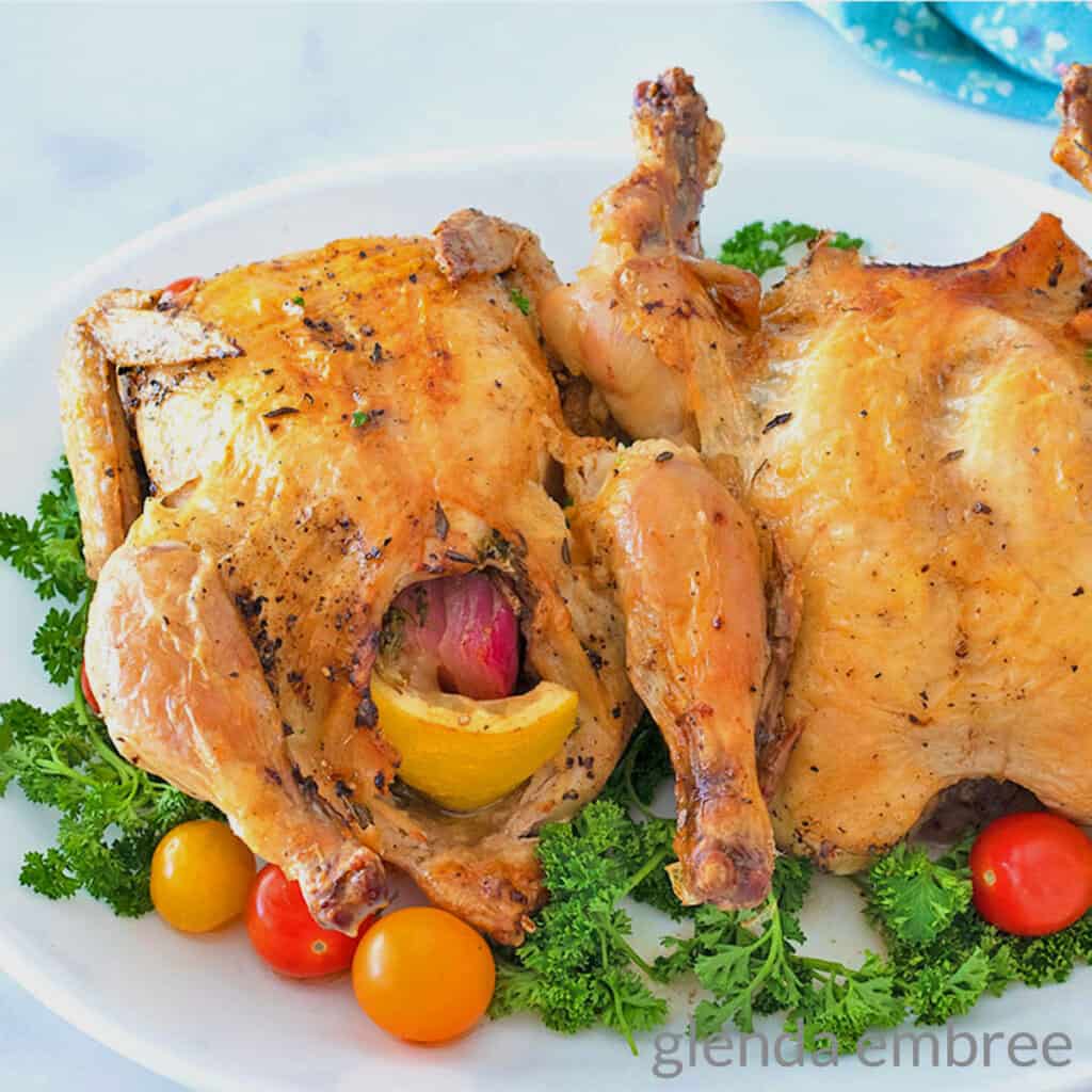 2 Air Fryer Cornish Hen on a white platter garnished with parsley and grape tomatoes.