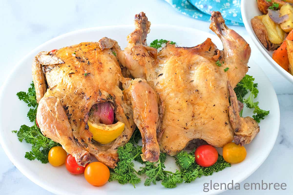 2 Air Fryer Cornish Hen on a white platter garnished with parsley and grape tomatoes