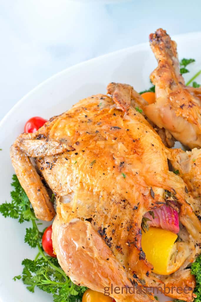 Air Fryer Cornish Hen on a white platter garnished with parsley and grape tomatoes
