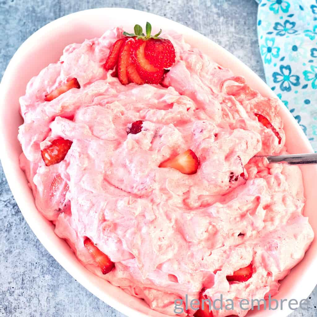 Pink Strawberry Cottage Cheese Salad in a white oval bowl. There is a sliced strawberry garnish at one end of the bowl.