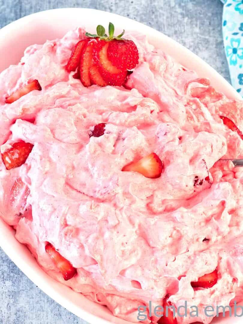 Pink Strawberry Cottage Cheese Salad in a white oval bowl. There is a sliced strawberry garnish at one end of the bowl.